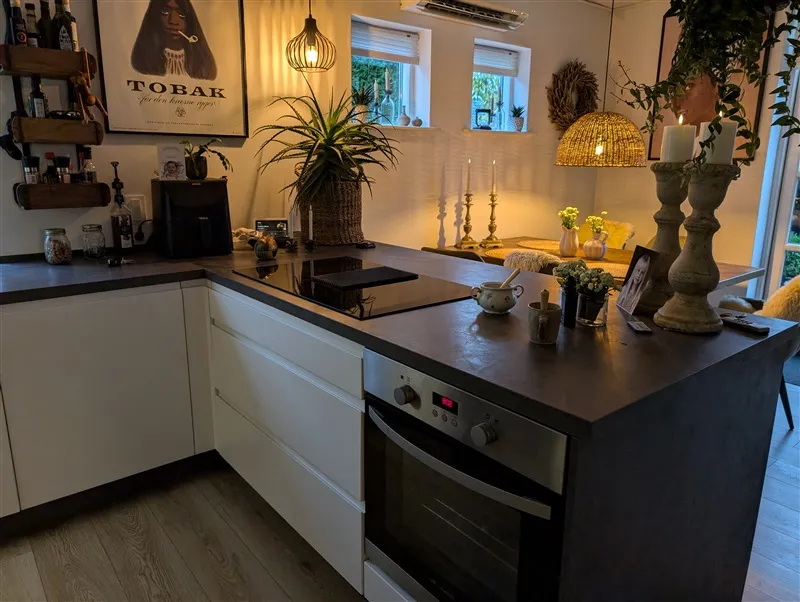 Køkken med en stor sort ø, en ovn, et bord med puder og et billede af Tobak på væggen