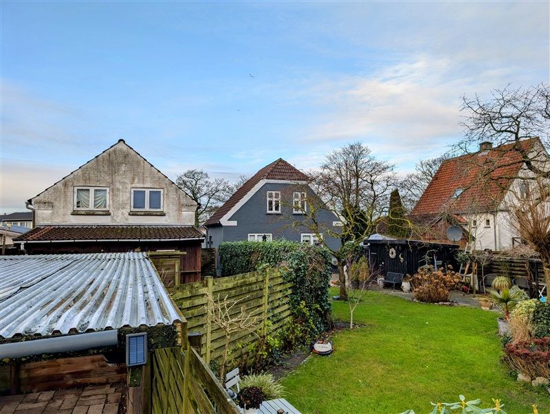 Have med græsplæne og en række huse i baggrunden i et landsbyområde med lyseblå himmel og skyer