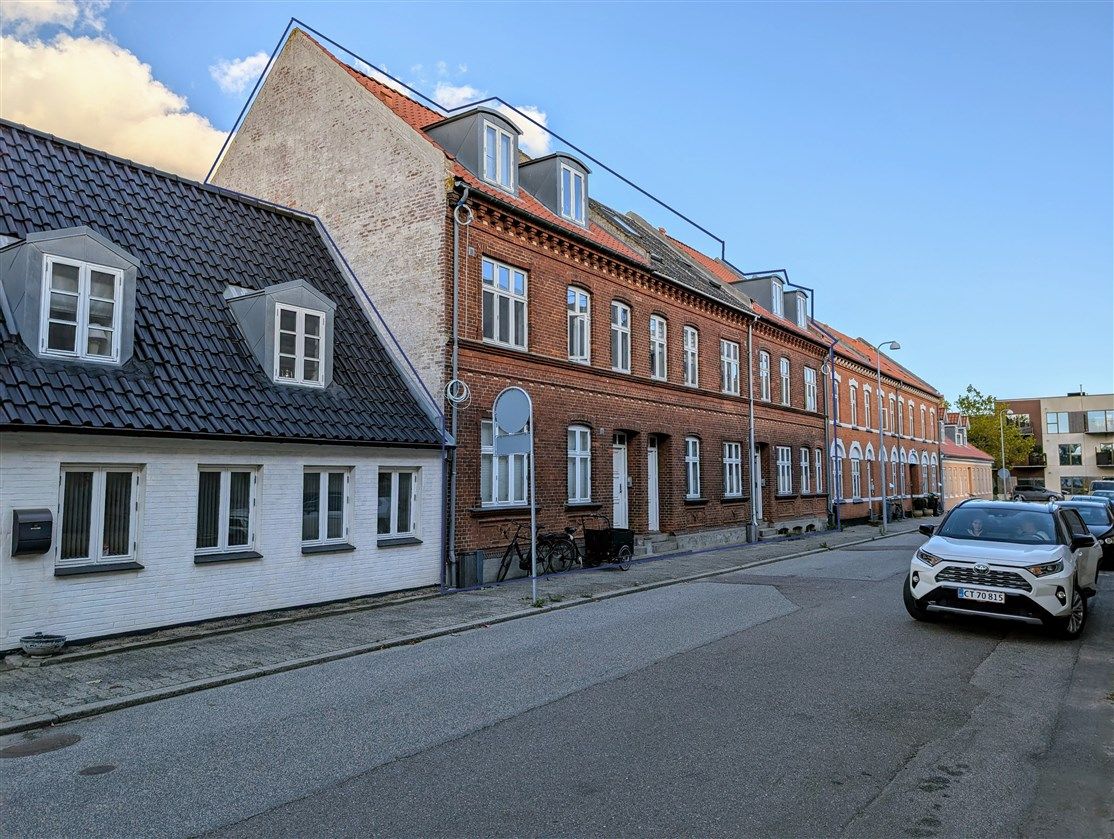 Solskinskindere på gaden med røde og hvide bygninger og biler parkeret langs siderne