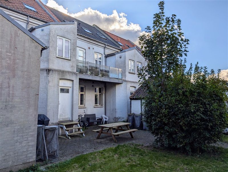 Moderne huse med balkon og trapper uden for. Smukt grønt græs, træbænke og planter. Solskinsstråler skinner gennem skyerne.