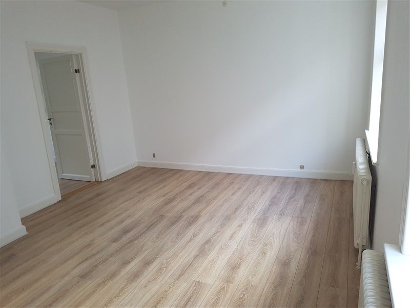 Et tomt rum med hvide vægge og en hårdt trægulv, hvor en hvid radiator står ved væggen