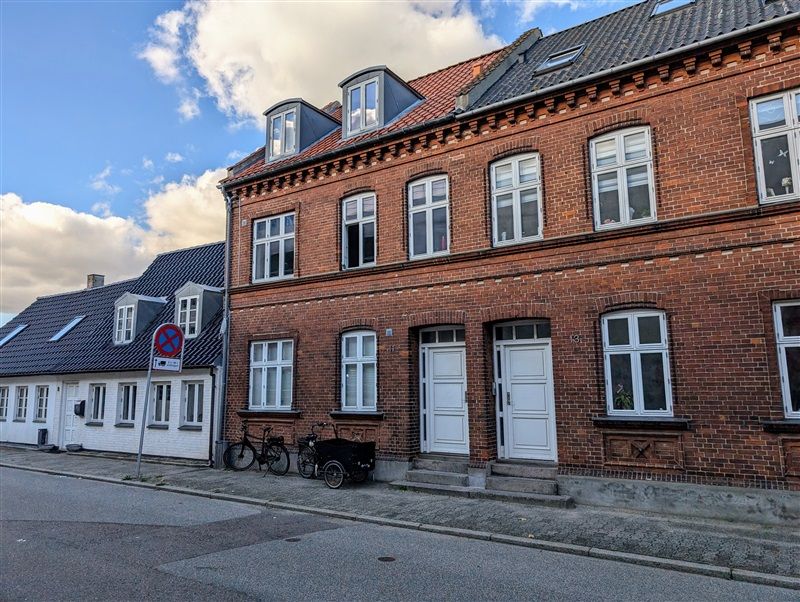 To huse med røde mursten og hvide rudevinduer på Sundegade i Fredericia. To cykler og en vogn står foran et af husene.
