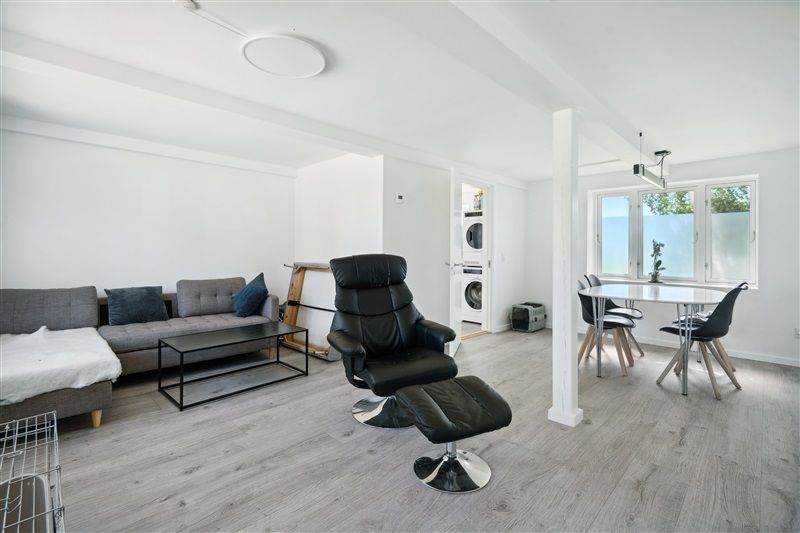 Rent lyse og moderne stue med sofa, lænestol, fodstol og spisestue med borde og stole. Stuen er udstyret med hvidt loft,