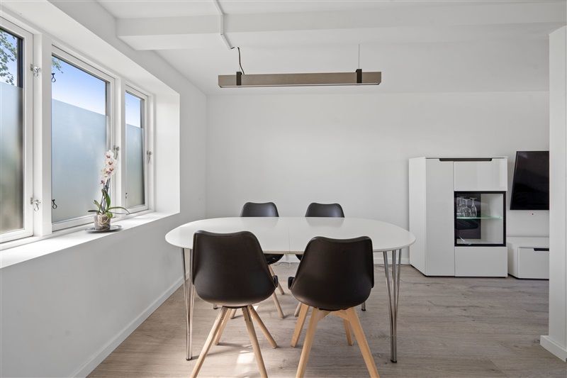 Minimalistisk spiseplads med hvide vægge, lysegrå gulv og runde højstole samt et rundt bord