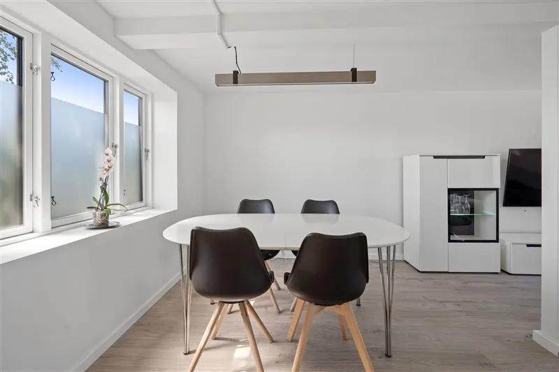 Minimalistisk spiseplads med hvide vægge, lysegrå gulv og runde højstole samt et rundt bord