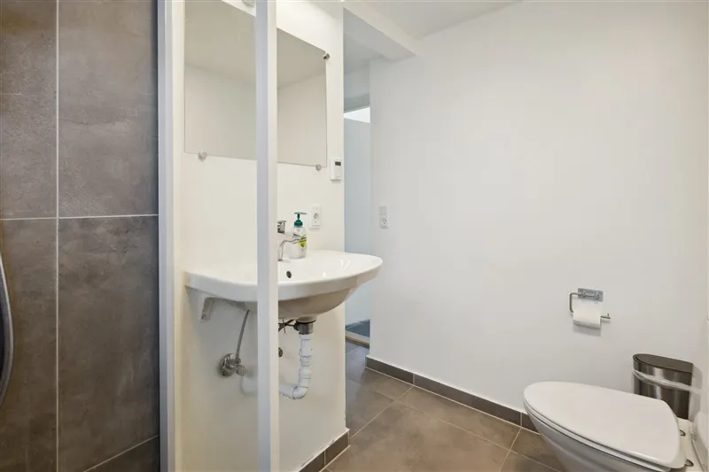 Et lille, lyse og rent badeværelse med hvidt toilet, en hvid vaskebækken og to spejle på væggen