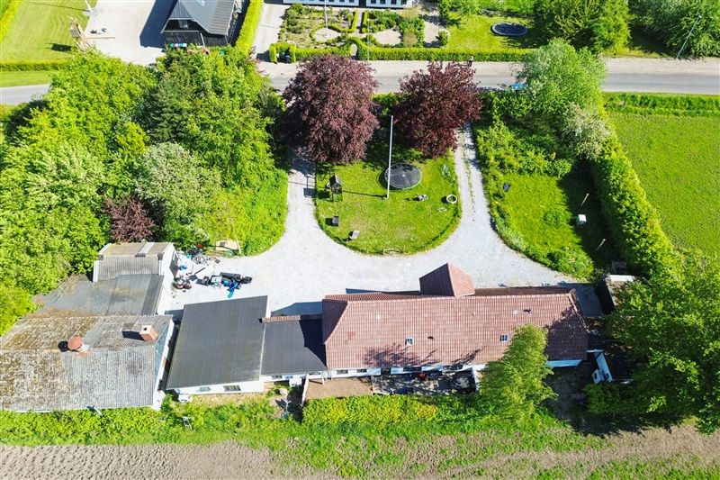 Investeringsejendom i Hejsager med gårdhave, haver og træer, både til venstre og højre for vejen og i baggrunden.