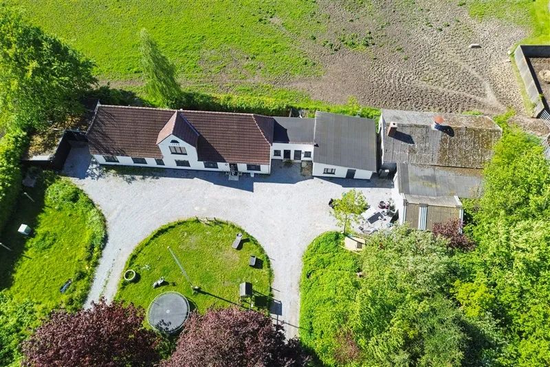 Et stort hvidt hus med brun tagbelægning og en udstrækning mod højre med en stor garage og et højhus