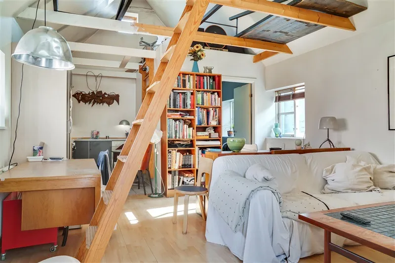 Et skandinavisk indretningsværelse med højloft, lyse trægulve, hvid sofa, lysegrå tæppe, massivt træbord og smuk