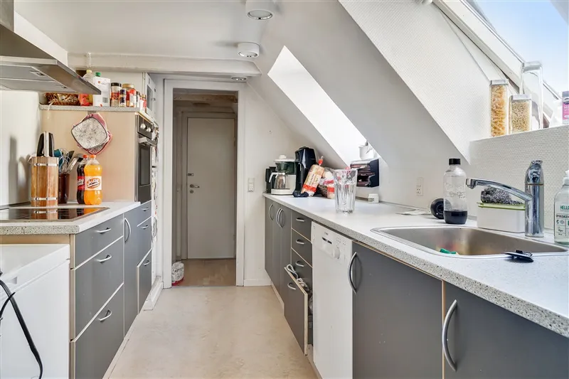 Moderne køkken med lyse loftsvinduer, hvidt og gråt køkkeninventar, strygejern og brætter på væggen og en køkkenø