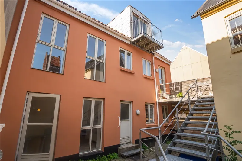 Kig på den orange udlejningsejendom med lyseblå rude og lysegrå døre. Ejerskabet er præsenteret af DK-Estate Erhvervsmægler.