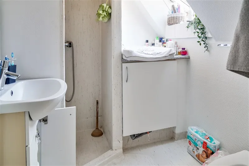 En lille badeværelse med hvidt badekar, hvidt vasketøjsskab og en hængende grøn plante.