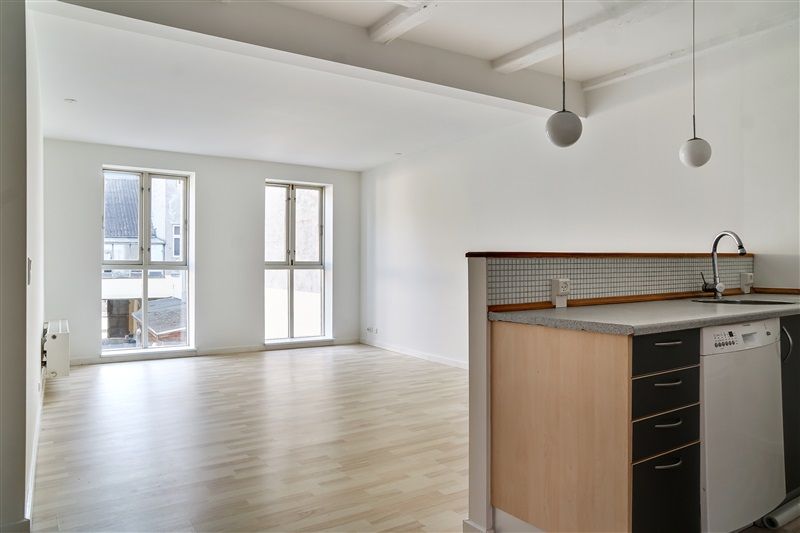 En tom køkken med trægulv, hvide vægge og to runde loftslampe i hvidt. Et træskabsskab med hængslede døre og en hvid