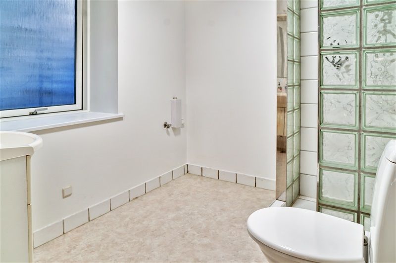 Foto af et lukket badeværelse med hvidt loft, vægge og gulv og et vindue med udsigt til byen