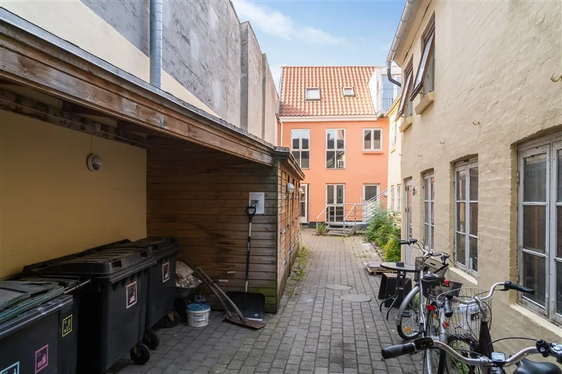 En smal, lille gyde med gamle bygninger og fiksede cykler parkeret på siden. To søsterhus i orange og lysegult står i
