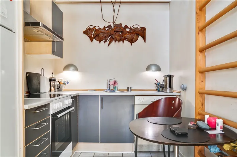 En lille køkken med rustne dekorative væghængere, to stole og en rund bord med telefon og glas på.