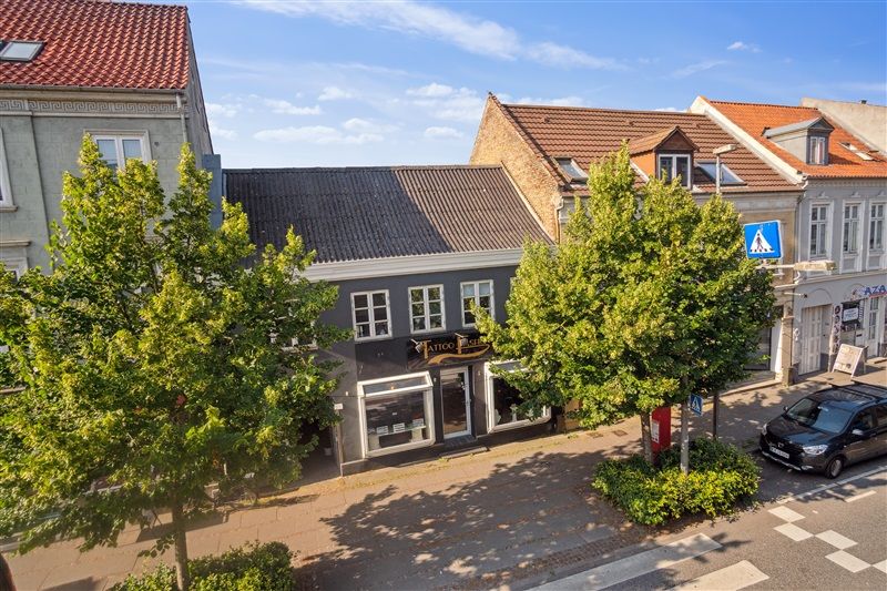 Udlejningsejendom Nørregade 26 i Horsens med flere butikker og parkerede biler på gaden
