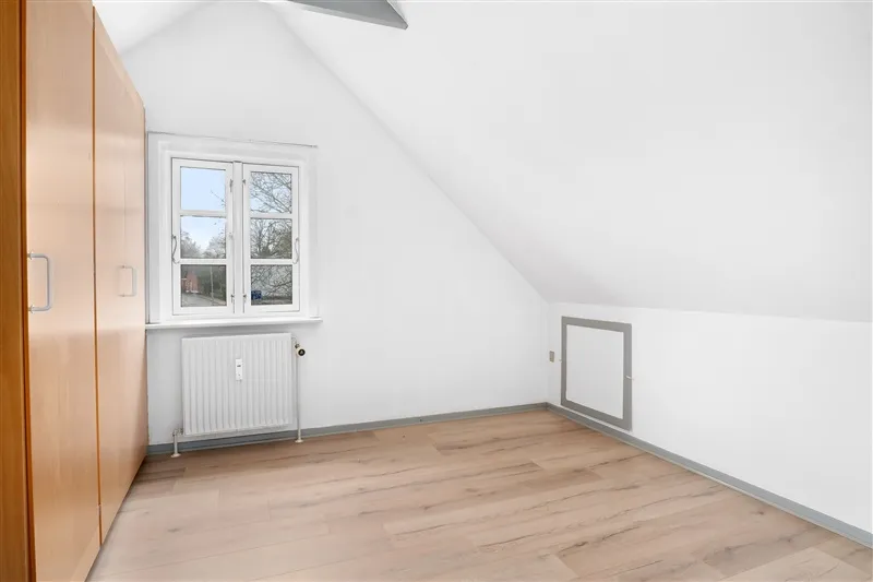 En hvid stue med lyse trægulve, en hvid væg og en hvid rude i vindue med en træskab og en radiator i rummet