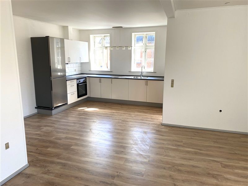 Nyt og rensynet køkken med højloft, hvide skabe, massivt trægulv og moderne hvide apparater