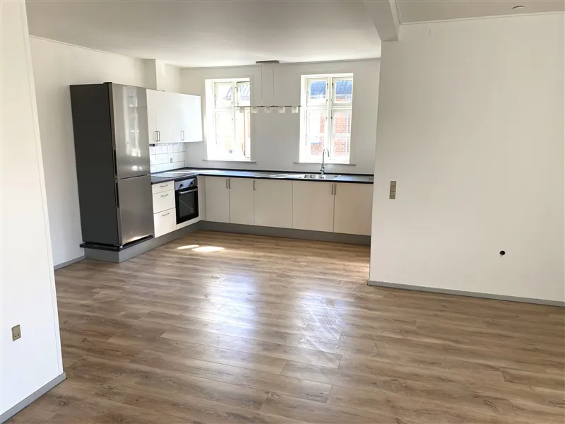 Nyt og rensynet køkken med højloft, hvide skabe, massivt trægulv og moderne hvide apparater