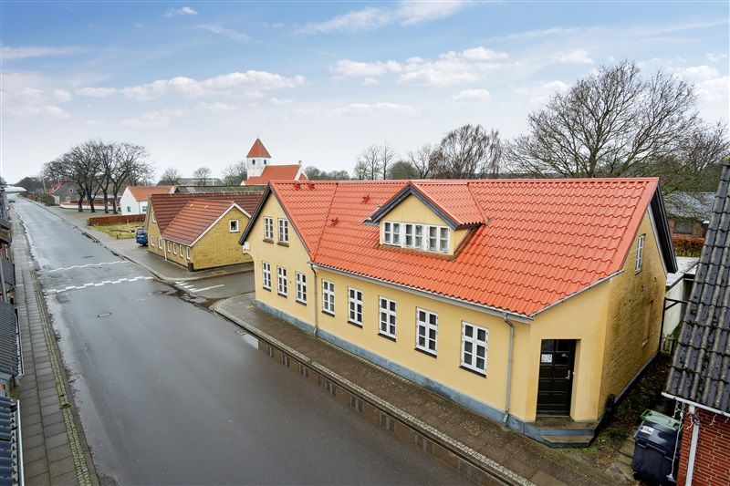 Gule huse med røde tag i Skovlund, Ansager, med små haver og kirke i baggrunden