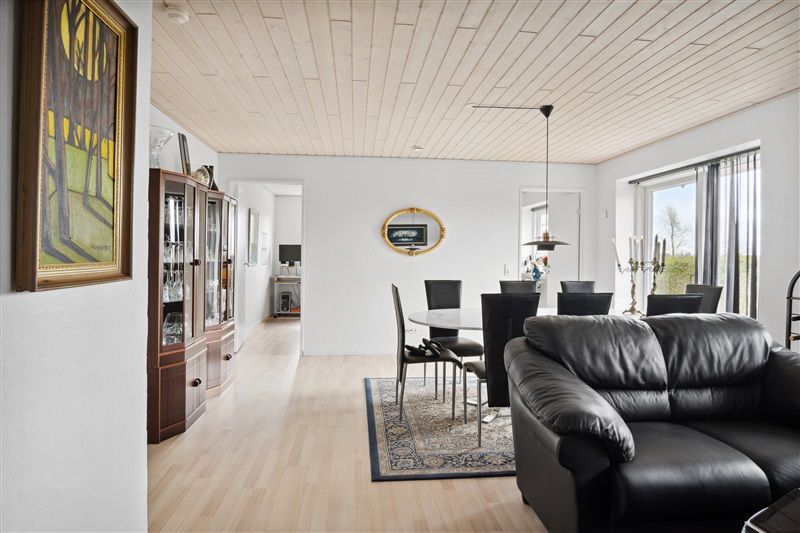 Moderne stue med højt loft og lyse trægulve, runde spisebord med stolpelampe, gult spejl og sort lædersofa
