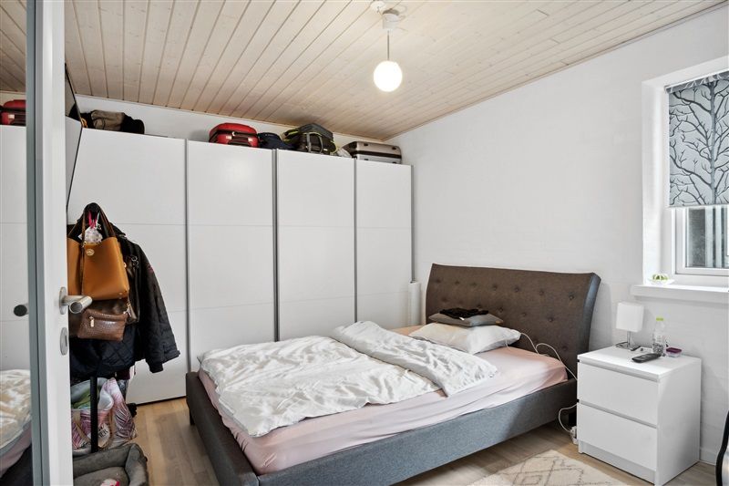 Soveværelse med dobbeltseng og højt loft, hvor der er to store hvide skabe og flere stykker rejsetasker