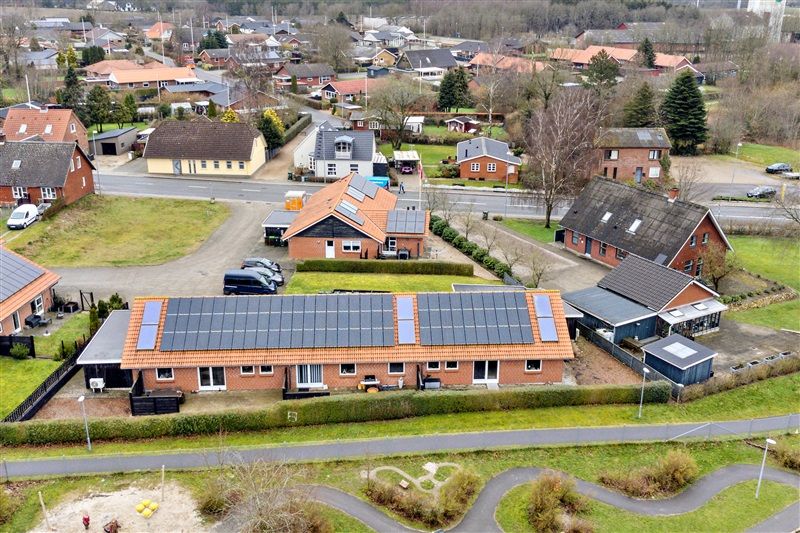 En rækkehuse med solceller på taget og to biler parkeret i garagen