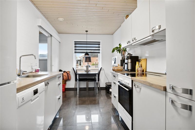 Moderne køkken med hvidt loft, hvide vægge, hvide skabsfronter, lysegult gulv og hvide møbler med sort stålhåndtag