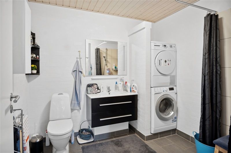 Bad med hvidt toilet, hvidt vask og lysegråt håndklæde på væggen