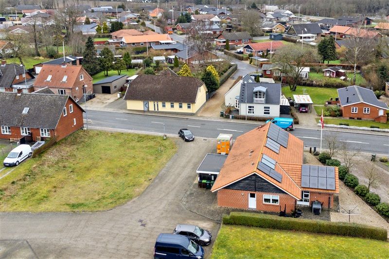 Et foto af flere rækkehuse i et boligområde med solceller på nogle tag. Der er en gårdsplads med biler og en bus parkeret på