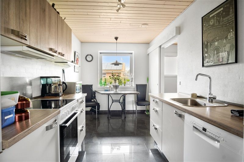 Moderne køkken med hvide skabe, sort ovn, vaskemaskine, bord, stol, plante, klok og maleri på væggen