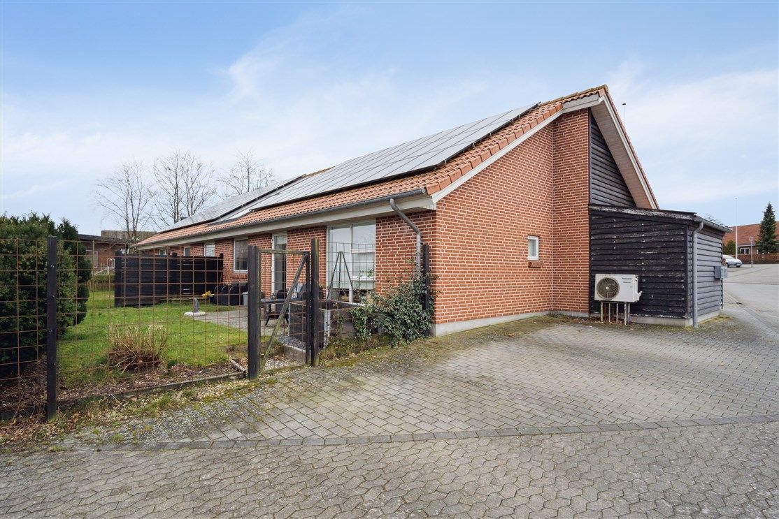 Rækkehuse med solpaneler på taget og gul vej med parkeringsplads og skur med klimaanlæg