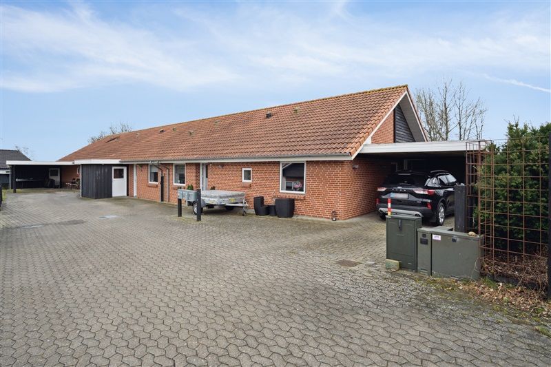 En ny rækkehuslejlighed i Hejnsvig med garage, bil og trailer parkeret foran. Der er et gitter og plante ved siden af.