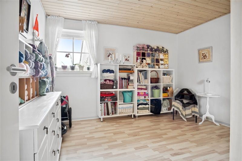 En hvid stue med hyggeligt møbleret indretning, masser af træ og højloftet med lyse, smukke møbler og vindue med gardiner