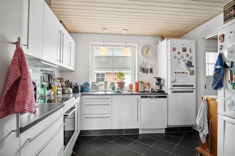 Et moderne køkken med hvide skabe og skarpe, sorte fliser på gulvet og loftet i lyse træplanker