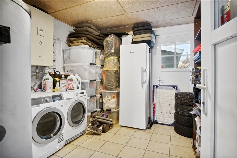 Moderne vaskeri med to vaskemaskiner, tørretumblere og et køleskab fyldte med diverse husholdningsartikler