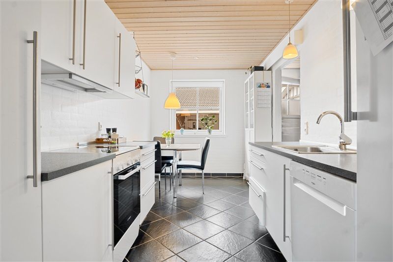 Moderne køkken med hvide vægge, sort gulv og hvide skabe samt bord og stole med plante i vase