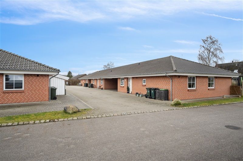 Moderne rækkehuse med garage og parkeringsplads udenfor, stående i række i forholdsvis fredfyldt område med grønne marker og