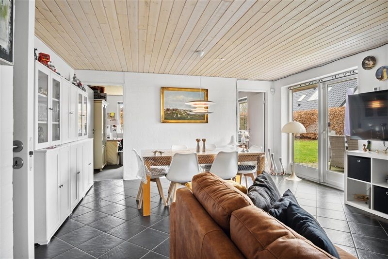 Et moderne køkken med lyse vægge og en stor spisebord med stole samt en tv-skærm og en sofa