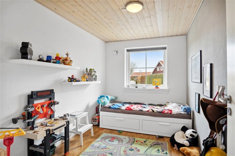 Et barneværelse med højt loft, et lægebord med mange legetøj og en lille panda på gulvet