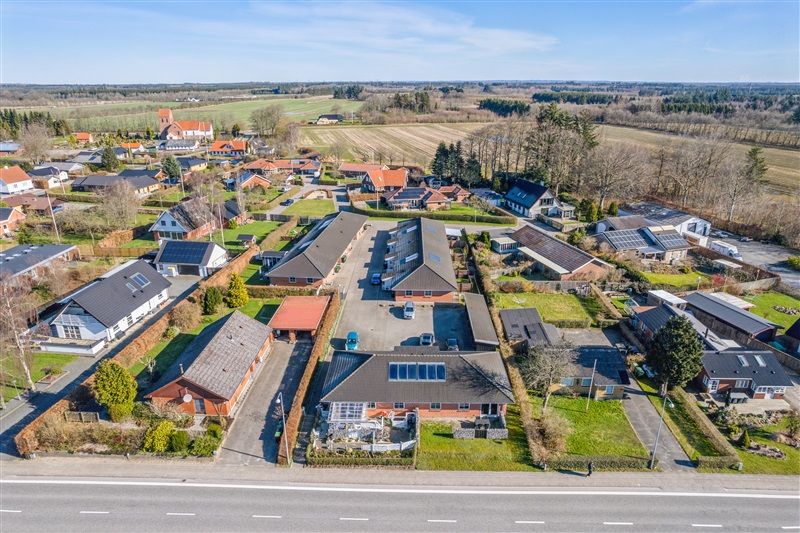 Moderne rækkehuse med solceller på tagene og parkeringspladser foran ligger ved siden af en bred asfaltvej