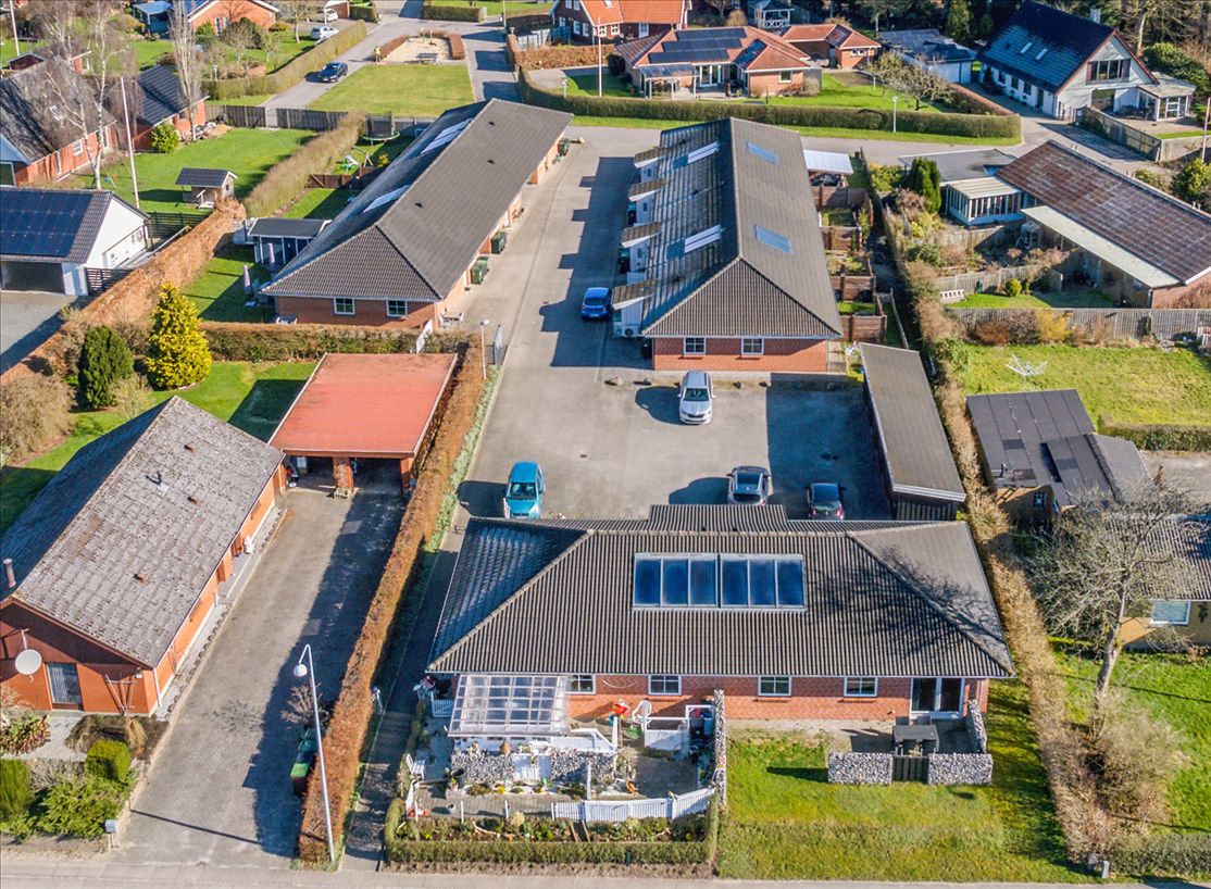 Flere moderne rækkehuse i en forstad, hvor de er omgivet af grønne haver og parkerede biler