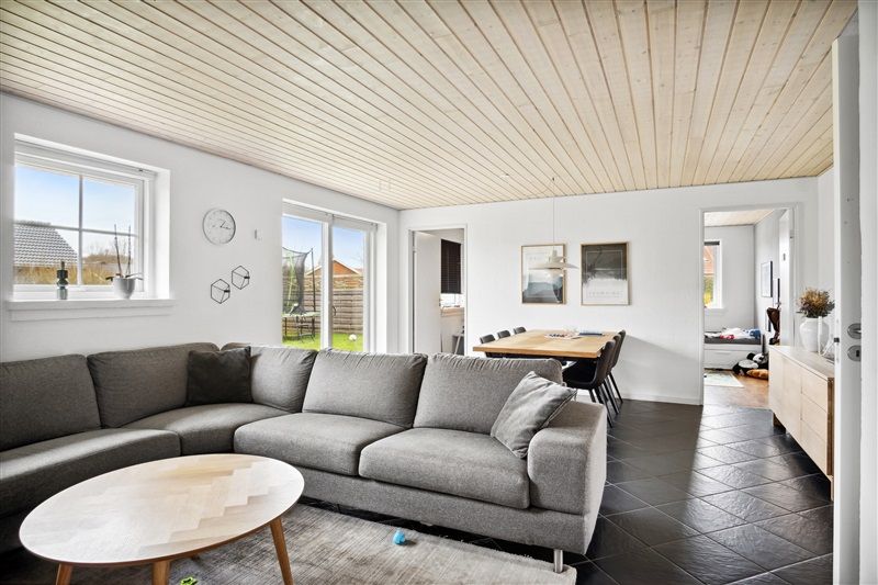 Moderne stue med hvid gulv, lysegrå sofa, rundt træbord, højt loft og hvide vægge med simpel indretning