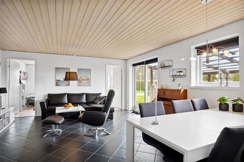 Moderne stue med højt loft og lyse vægge med sofa, bord og stole samt et køkken med moderne møbler og udendørs terrasse