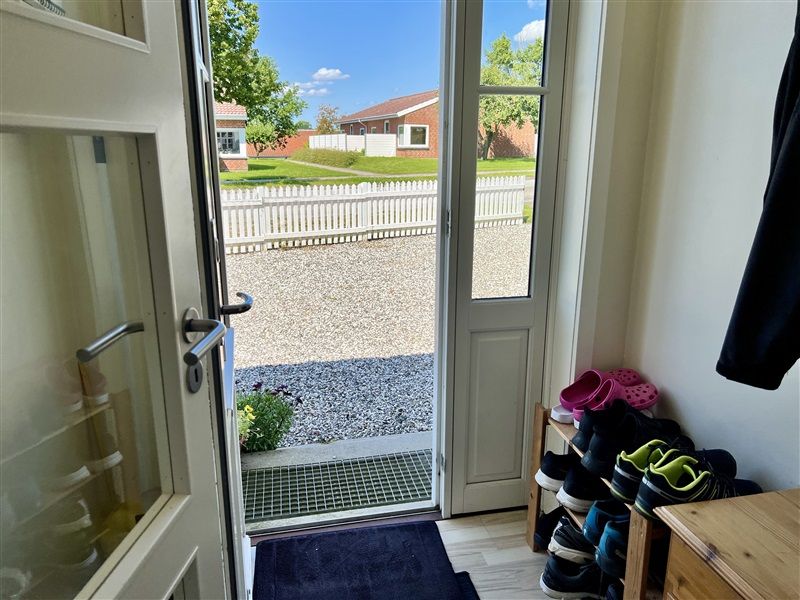 Lejlighed med trægulv og møbler, en række sportssko og sandaler samt et rek og en have med blomster og en hvid hegn