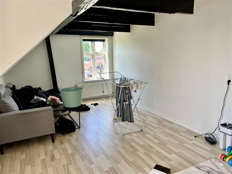 Lejlighed med lysegul væg og trægulv, sofa, vase med blomster og tøj på tørrestativ