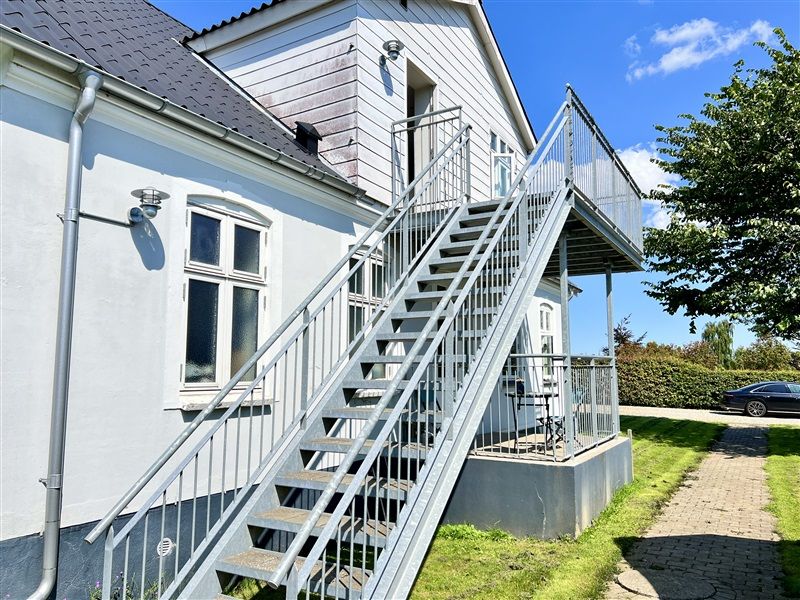 En moderne terrasse til en lejlighed med trapper og udsigt til have med træer og en bil parkeret på siden