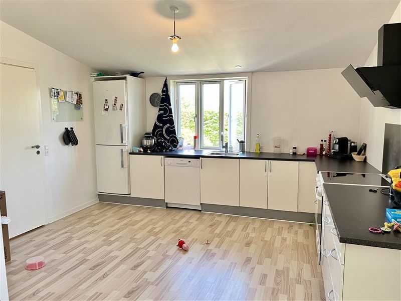 Moderne køkken med hvide vægge og lyse trægulv. Køkken med hvide skabe og sorte bordplade og hjørner. Køkken med moderne