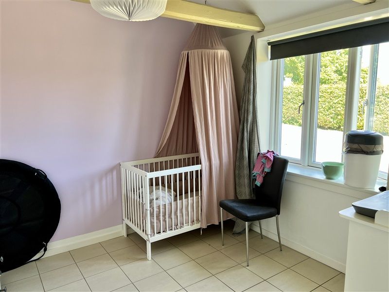 En børneværelse med lysgrå væg og hvidt barneseng, pink baldakin og mørkeblå stol ved vinduet